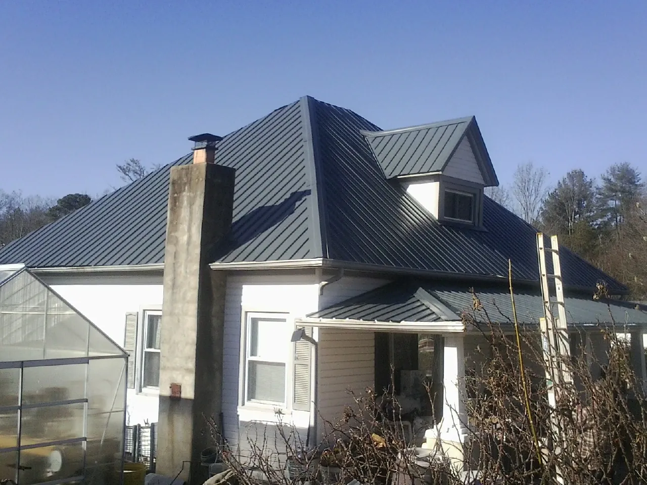 Dark blue standing seam metal roof on a white farmhouse with dormer — Slate & Tile Roof Repair by Roofing Brothers in Hogansville
