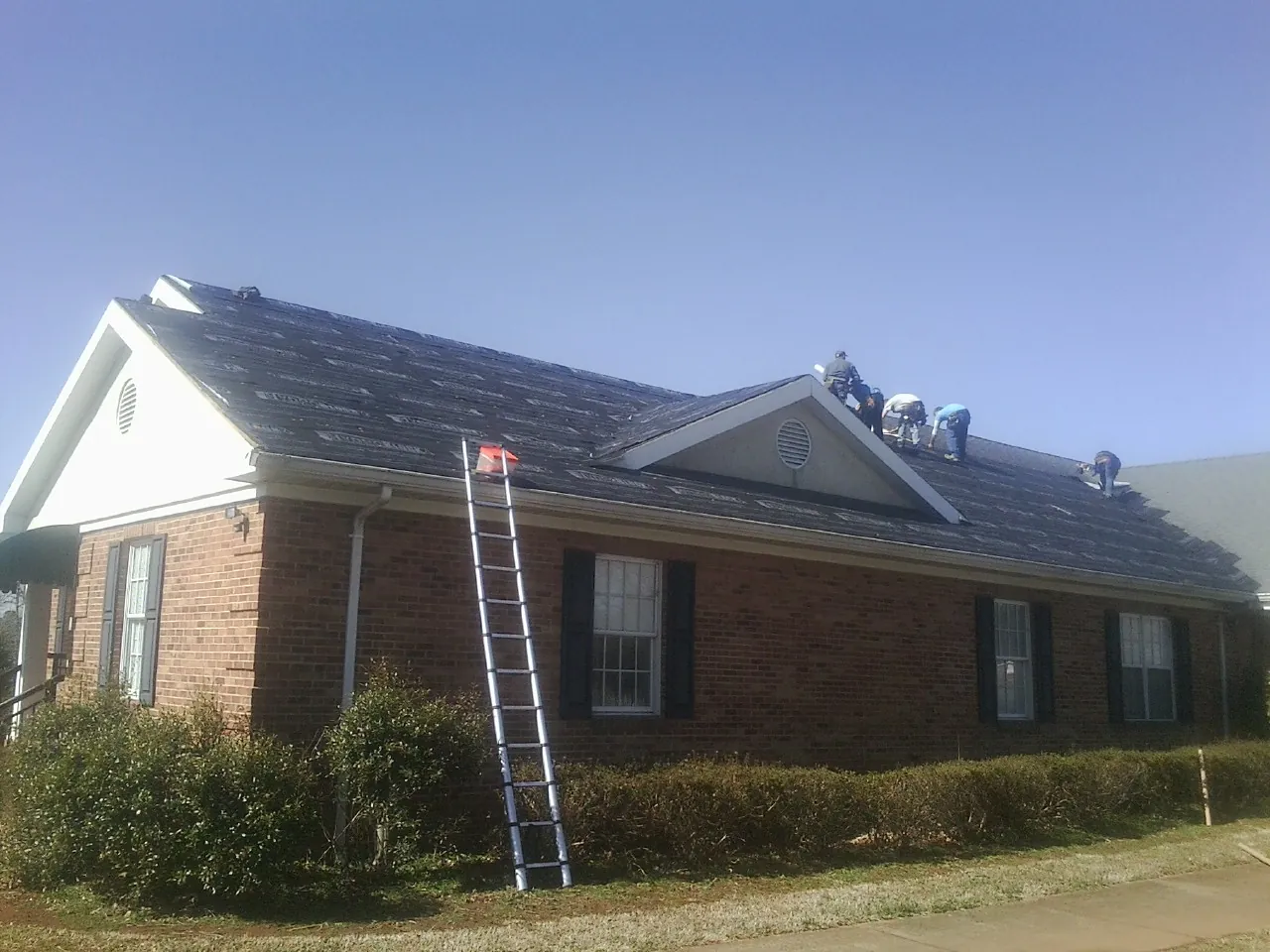 Crew tearing shingles off a brick ranch roof with a ladder set — Emergency Roof Repair work by our crew in Hogansville