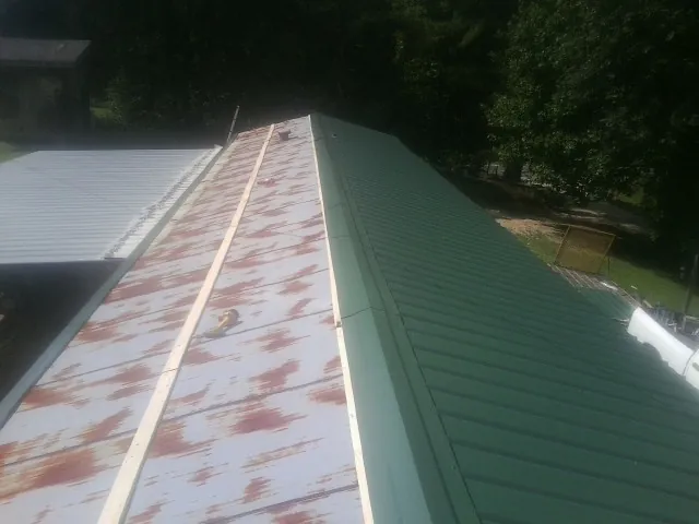 Old rusted panels beside newly installed green metal roofing — Wind Damage Roof Repair by Roofing Brothers in Hogansville