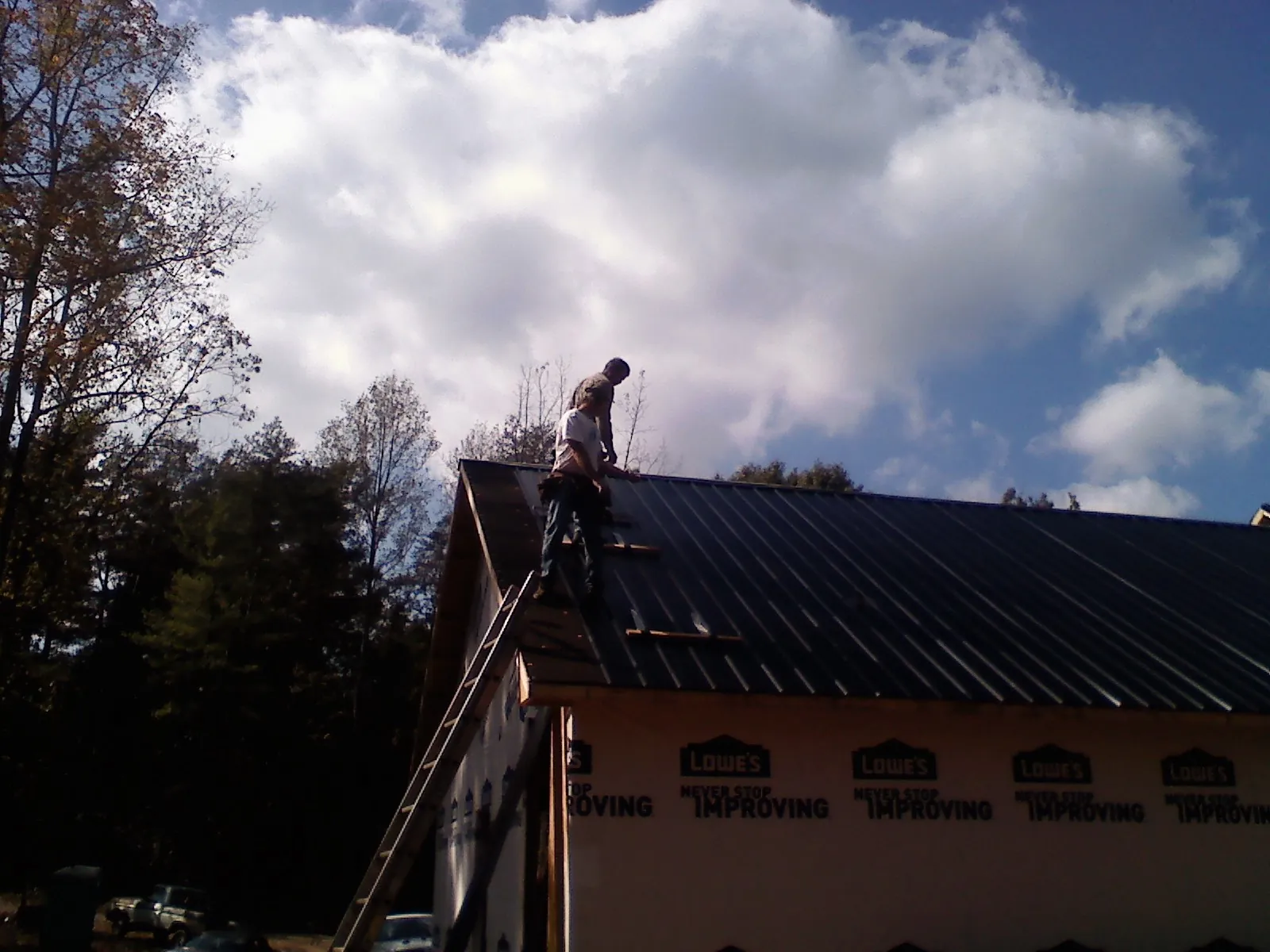Roofer fastening dark metal panels high against a cloudy sky, from a Roof Inspection job in Hogansville