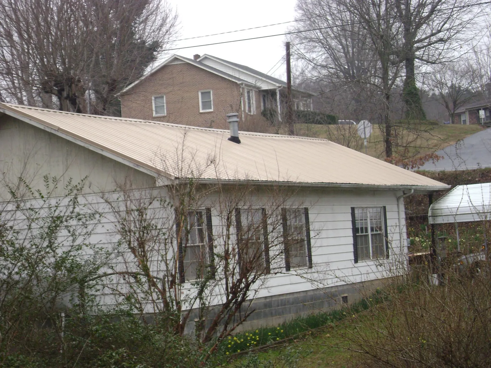Tan metal roof on a white sided house set into a hillside — Commercial Roofing by Roofing Brothers in Hogansville